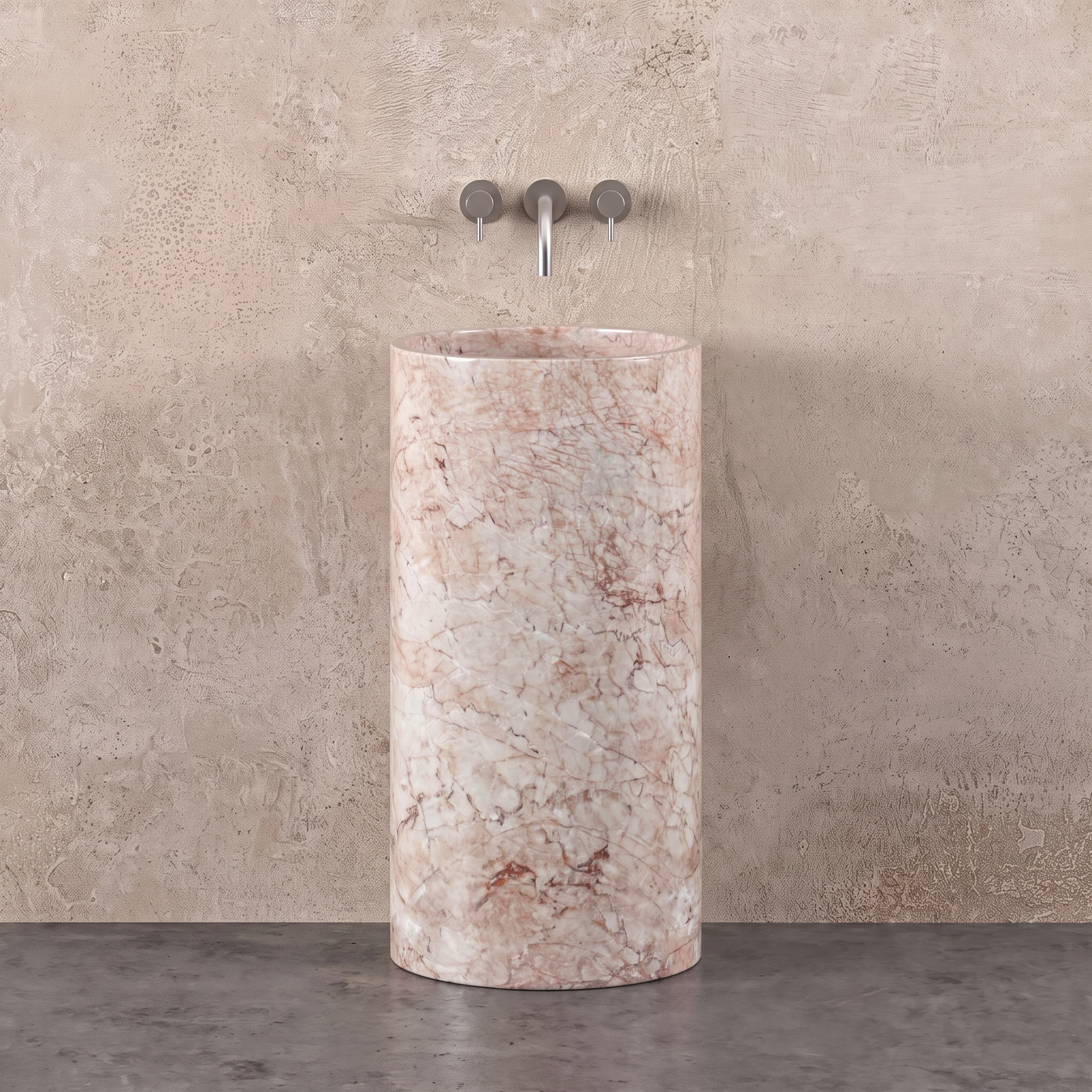 A tall cylindrical pedestal sink made of pink and white marble, set against a textured beige stone wall with a chrome three-hole faucet.